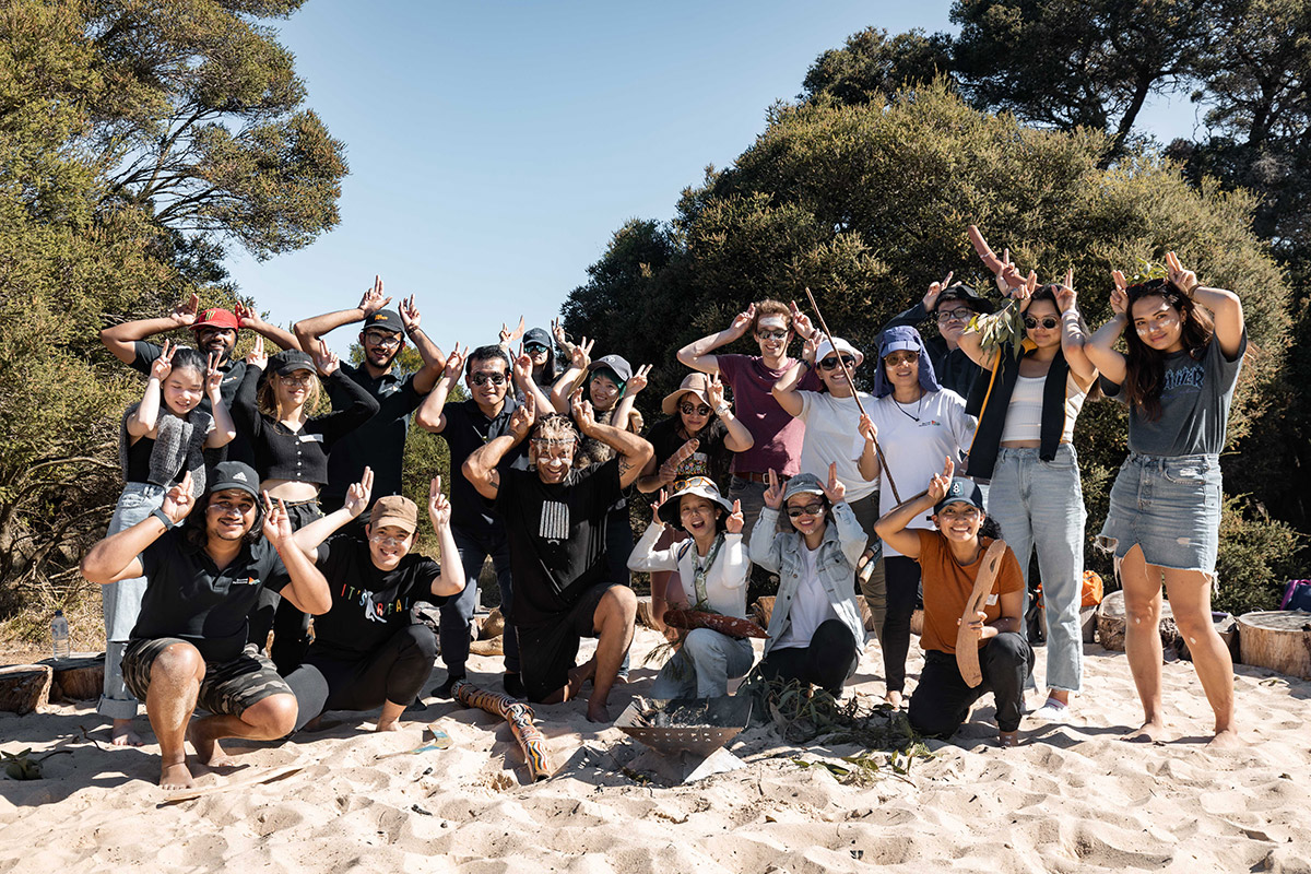 A large, diverse community group posing together on a beach after an activity