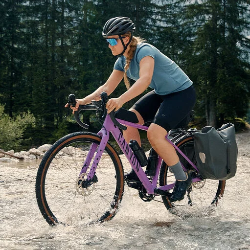A cyclist riding a gravel bike with pannier bags through a shallow water crossing