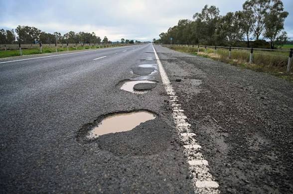 A chain of water-filled potholes along a highway shoulder