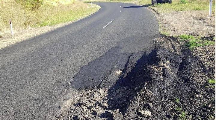 A rural road with a wide shoulder failure where the pavement has broken away from the edge
