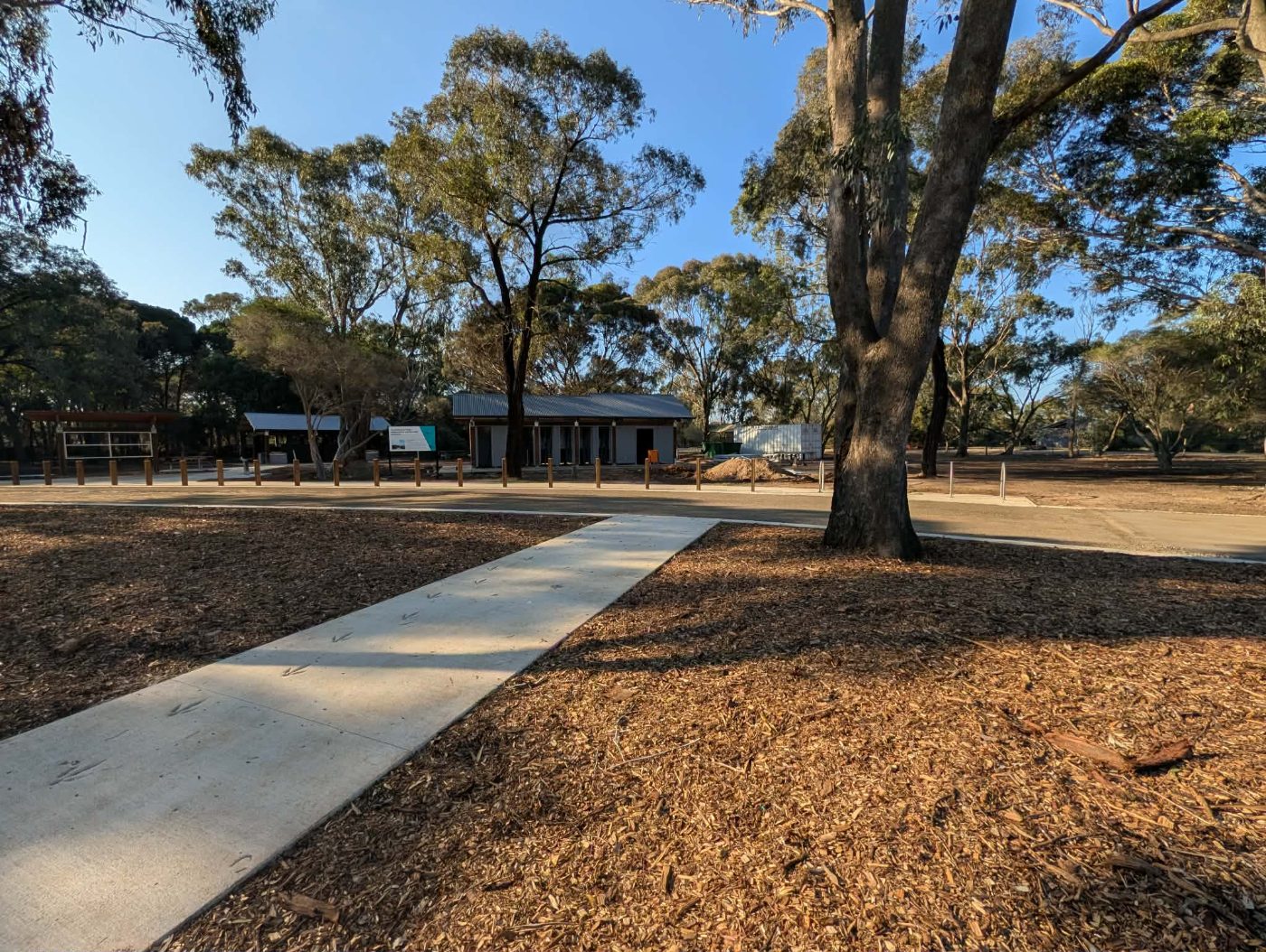 New concrete path leading across mulched garden beds toward the completed visitor building