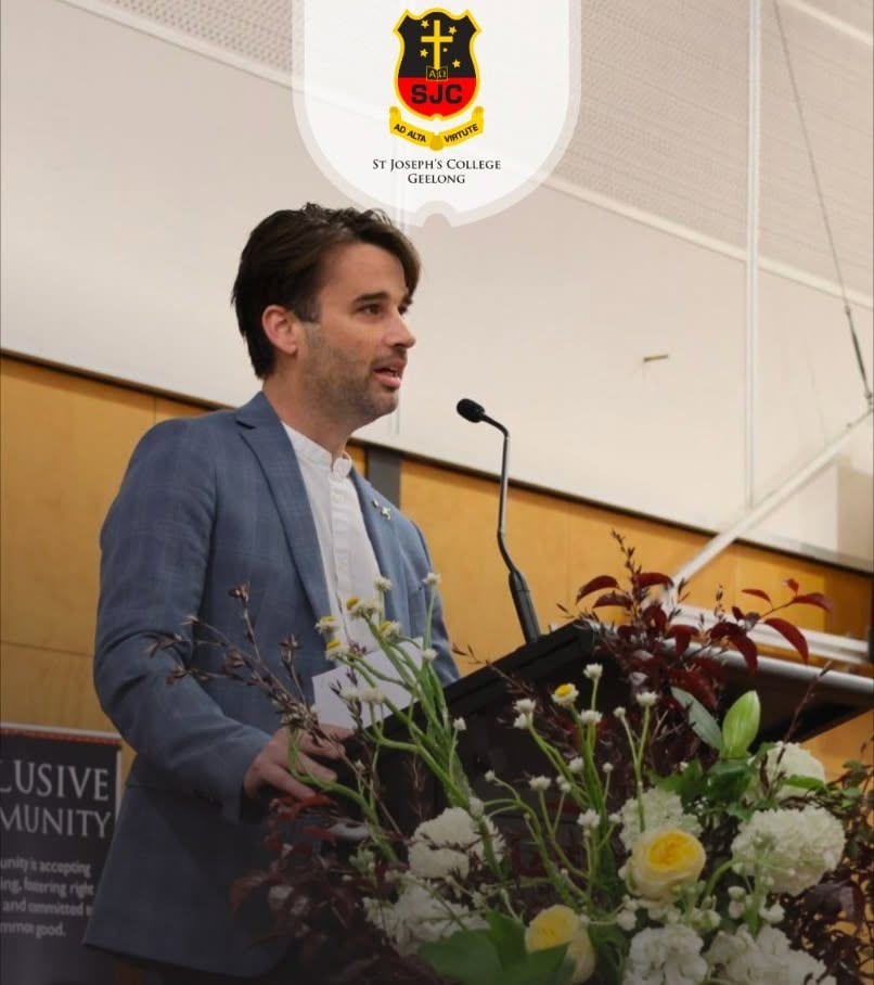 David Greenwood OAM speaking at a lectern at St Joseph's College Geelong, with the school crest displayed above