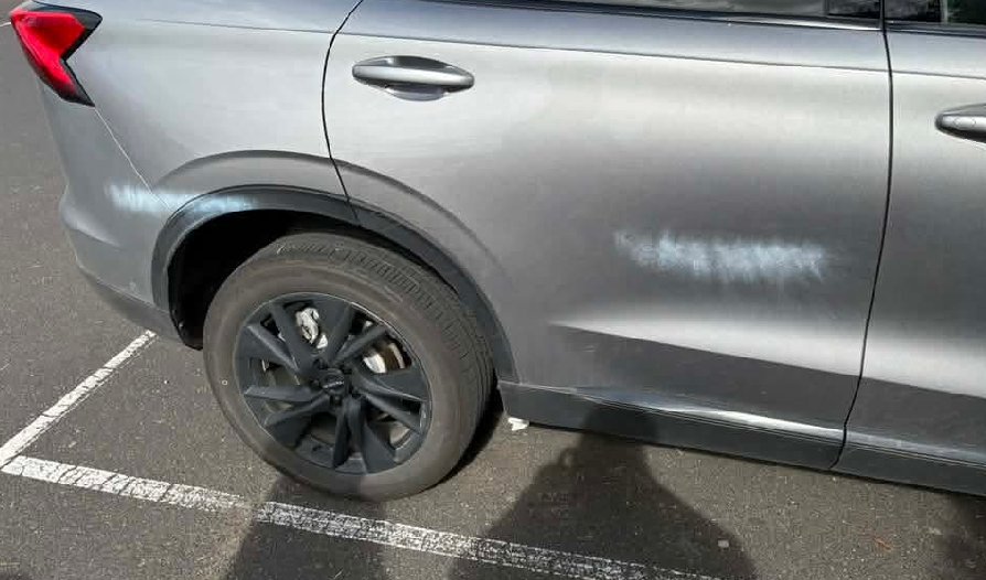 A silver SUV in a marked parking bay with a band of overspray along the rear door