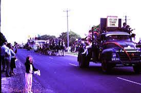 The parade from the kerb — a truck float, a crowd, and a child stepping into the road for a better look.