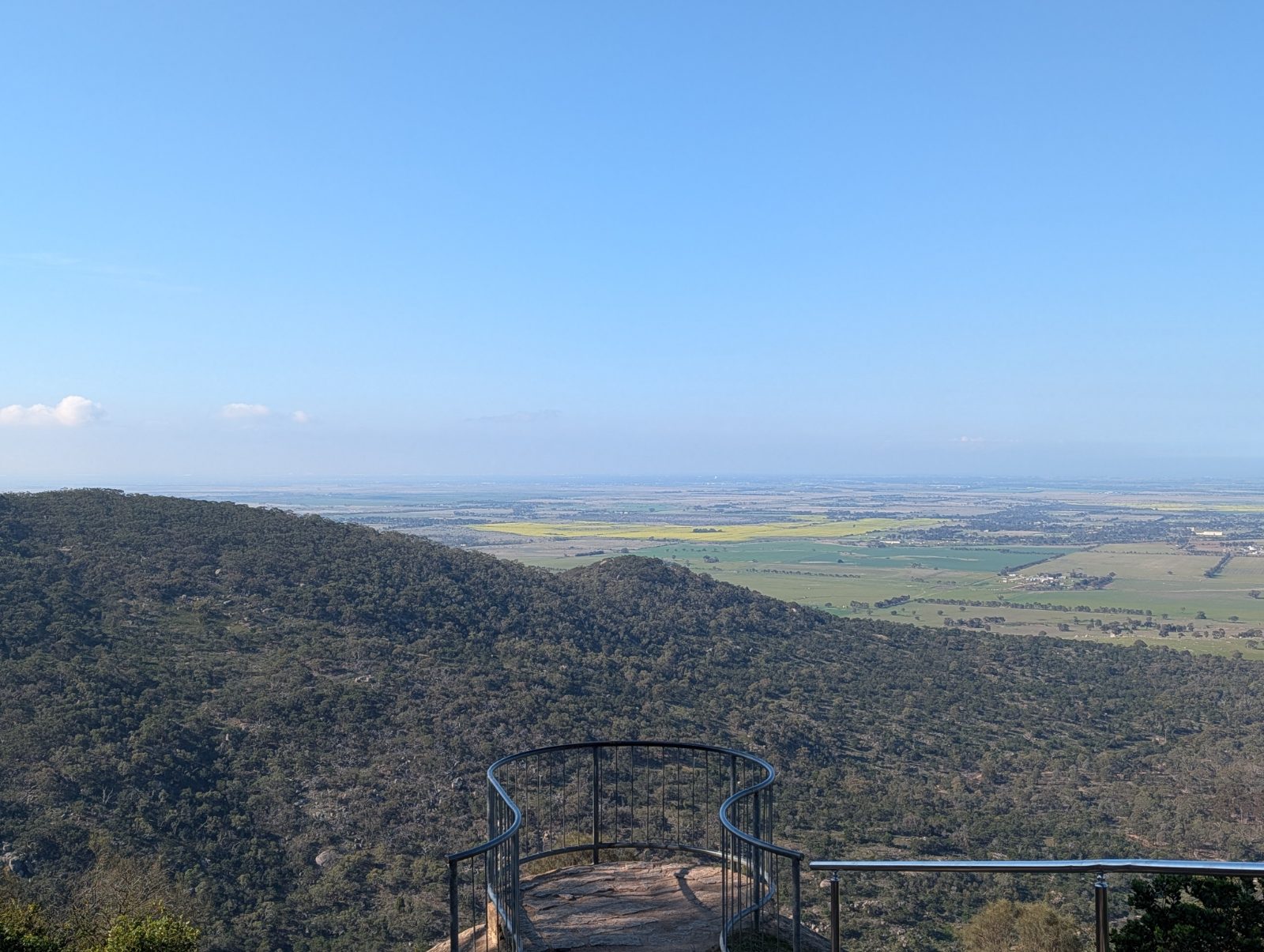The view from a You Yangs lookout platform across forested ridges to the canola paddocks and plains beyond